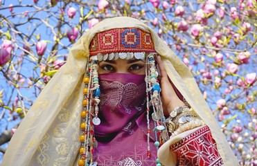 Girl against of magnolia flowers in national Palestinian costume, with head covered. 