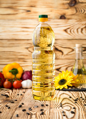 Bottle of sunflower oil on a wooden table with a composition of vegetables in the background