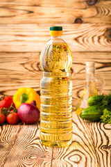 Bottle of sunflower oil on a wooden table with a composition of vegetables in the background