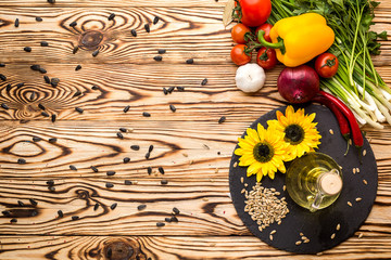 Glass bottle of sunflower oil on a wooden table with a composition of vegetables and seeds. Top view