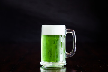 A stein beer mug with green beer on rustic wood table.