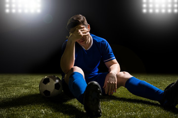 Footballer disappointed sitting on the grass field