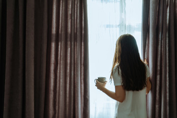 woman stand near window and drink coffee in the morning