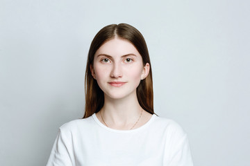 Model portrait without make-up in a white t-shirt on a white background. The girl poses in studio, smiling looking at camera. close up