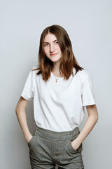 Obraz premium Model portrait without make-up in a white t-shirt on a white background. The girl poses in studio, looking at camera with serious or pensive expression