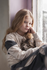 Cute little girl sitting by the window with fluffy cat