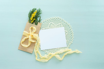The concept of international women's day Mimosa brunch in Kraft envelope bag on a blue background, the bow of yellow silk with white blank card for text, crochet doily