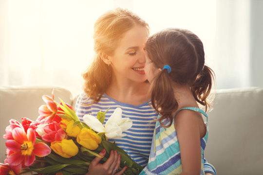 happy mother's day! child daughter   gives mother a bouquet of flowers to tulips and gift.