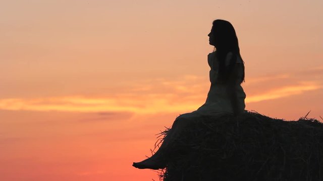 Beautiful woman silhouette sitting on straw ball admire nature at sunset