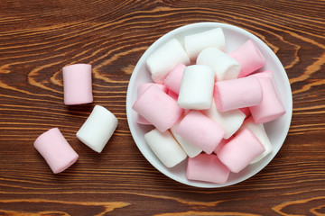 White and pink marshmallow on a saucer on the dark wood table