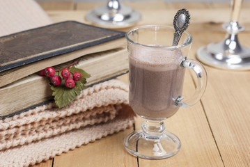 cup of cocoa stands on a wooden table , next a book with leaves
