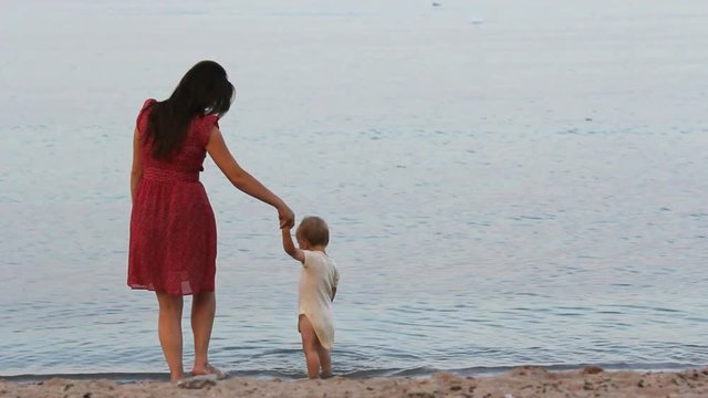 Mother and baby slash water sea, slapping with feet, have fun