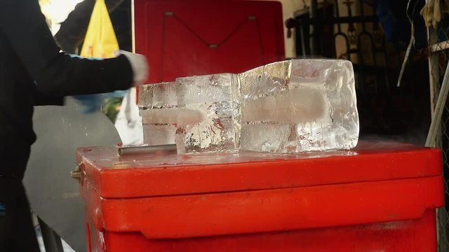 Ice seller cutting small blocks of ice with his hatchet and keeping it in plastic bags ( close up)