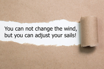 Motivational quote You can not change the wind but you can adjust your sails, appearing behind torn paper.