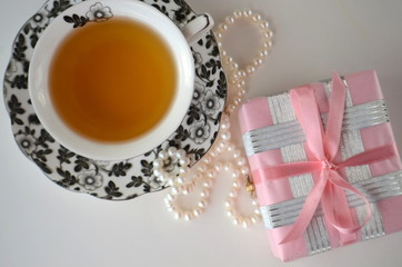 Gold and pink French macarons, chocolates with a cup of tea, pearls and an elegant pink gift-wrapped box. Luxurious gift. 
