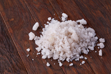Pile of salt crystals on the dark wooden background, top view, flat lay, shallow depth of field