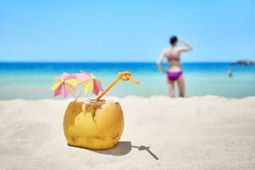 Coconut with colorful umbrellas and straw on a beach, summer holiday concept, selective focus.