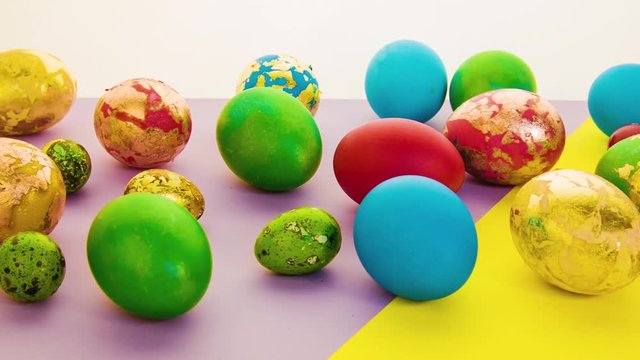 Beautiful multi-colored Easter eggs lie on a bright yellow and pink background in scatter. Small and large painted Easter eggs. Festive decoration for Easter.
