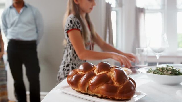 Girl brings and covers challah bread on table for Shabbat