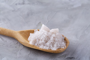 Crystal sea salt in a wooden spoon over light background, top view, close-up, selective focus