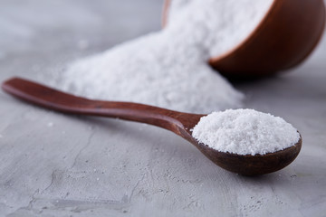 Composition of sea salt in ceramic bowl and spoon for cooking or spa on white background, top view, selective focus