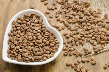 coffee beans in a white heart-shaped plate on the wooden table.
