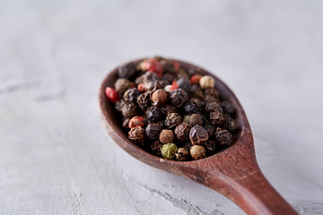 Peppercorns on wooden spoon over light background, top view, close-up, shallow depth of field.