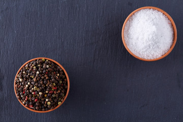 Conceptual composition of salt and pepper on spoons and bowls over dark background, top view, close-up