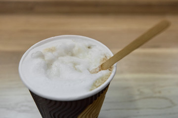 Cup of hot coffee with wooden stick to mix sugar, focus on the foam of coffee