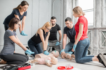 Group of people learning how to make first aid heart compressions with dummies during the training...