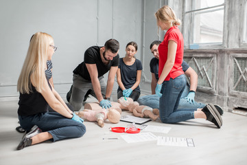 Group of people learning how to make first aid heart compressions with dummies during the training...