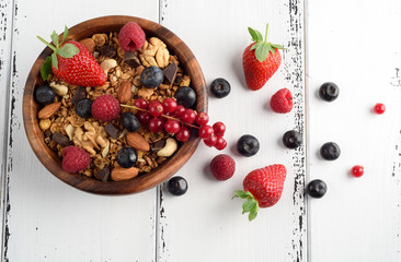 Bowl of homemade granola with yogurt and fresh berries on wooden background from top view