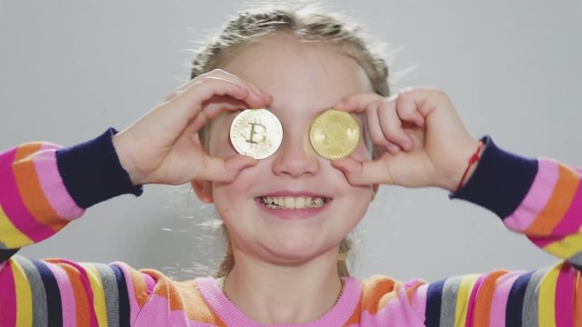  Girl holding a Golden Bitcoin in her hand,  looking at the camera and smiling