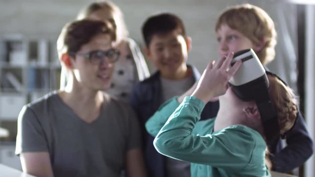 Teacher shows primary school children how to use virtual reality glasses during computer coding class, and they get excited