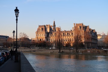 Fototapeta na wymiar Vue sur l’Hôtel de ville de Paris et la Seine depuis un quai, au soleil couchant (France)