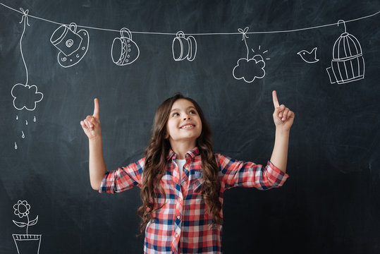 Vivid imagination. Cheerful creative little girl feeling happy while pointing her fingers up and showing lovely little cups hanging on a rope