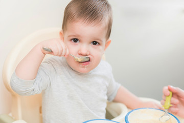 Fototapeta premium mom in the kitchen is feeding the baby milk porridge