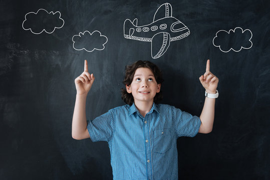 Lets fly. Excited cheerful little boy pointing to the sky while dreaming of travelling by plane