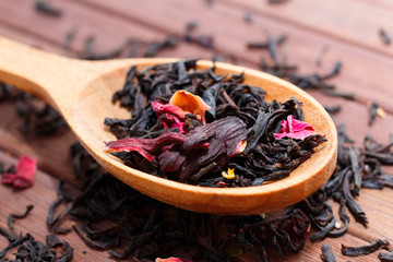 Composition of natural tea with a leaves of rose. Macro photo of tea petals on a wooden spoon with a rose. Tea with the ingredients of flowers and rose tea located on a wooden Board.