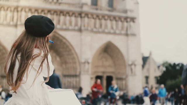 Cute little girl in beret sitting in crowded place and drawing. Brunette child near the of Notre Dame in Paris, France.