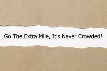 Fototapeta na wymiar Motivational quote Go The Extra Mile It's Never Crowded appearing behind ripped paper.