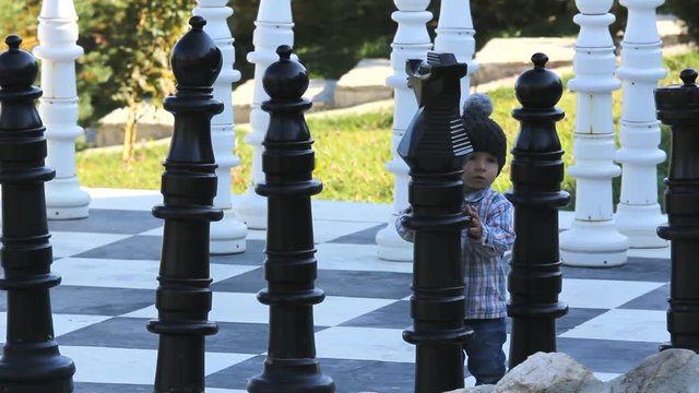 Lovely baby child looking to big chess pieces from a big chessboard 