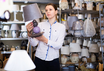 Woman is choosing new lamp for her home in the store.