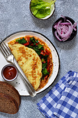 Homemade omelette with pepper and spinach for breakfast, on a gray, concrete background.