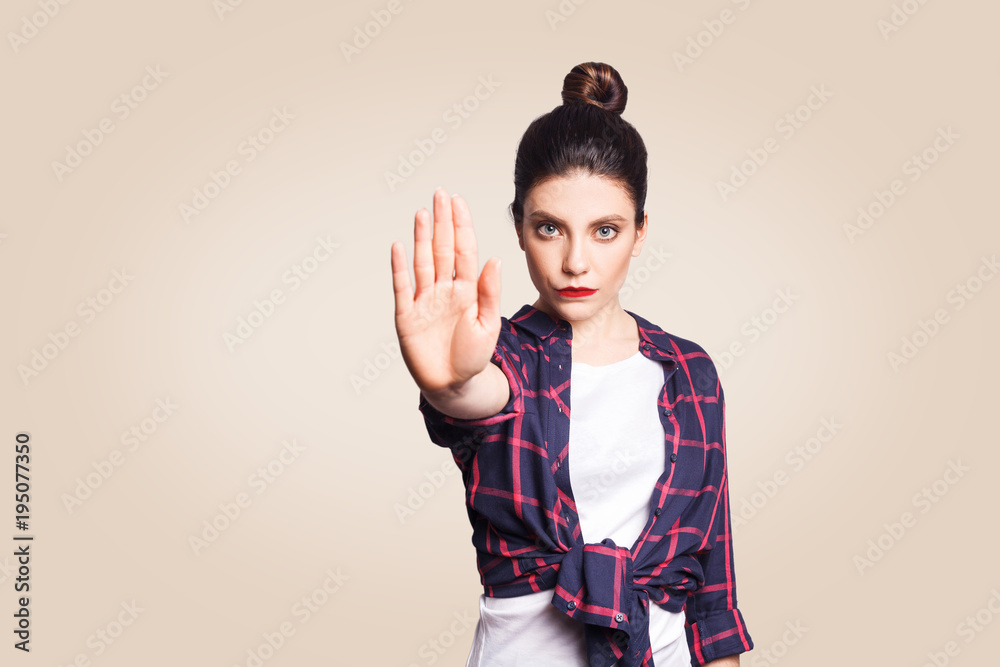 Wall mural Young annoyed woman with bad attitude making stop gesture with her palm outward, saying no, expressing denial or restriction. Negative human emotions, feelings, body language. Selective focus on face.