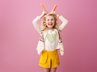 happy stylish girl on pink background making horns from carrots