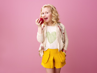 happy modern child isolated on pink eating an apple