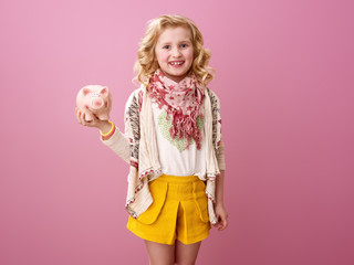 smiling modern child isolated on pink holding piggy bank