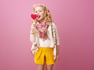 child isolated on pink background licking heart shaped lollipop