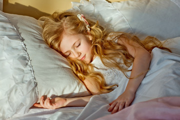 Cute little girl with long white hair, sleeping, smiling on bed at home in his room.